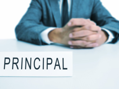 a man wearing a suit sitting in a desk with a signboard in front of him with the word principal written in it